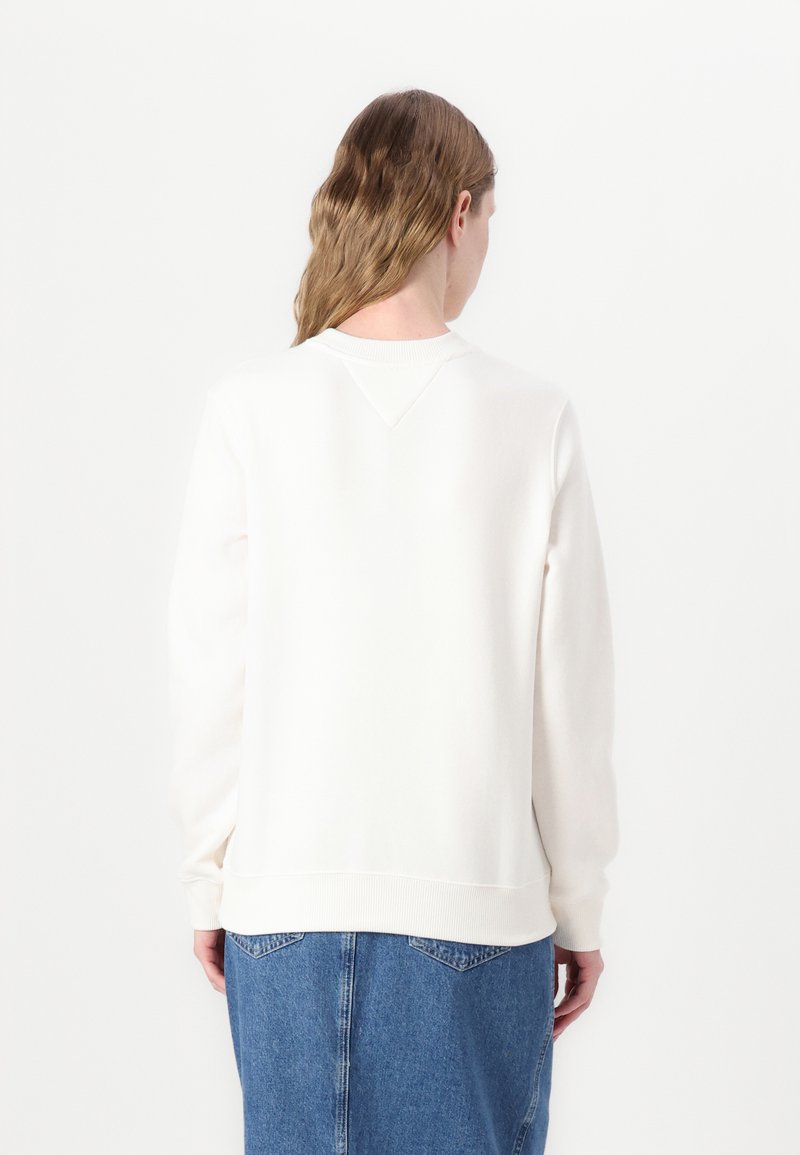 Sweatshirt blanc à manches longues, col rond et ourlet en côte. Texture lisse et douce. Porté avec une jupe en jean, vu de l'arrière.