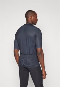T-shirt de sport bleu marine à manches courtes et col arrondi. Équipé d'un panneau arrière en maille et d'un ourlet élastique, associé à des leggings ajustés noirs.