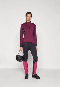 Αθλητική στολή που περιλαμβάνει μπορντό ζακέτα με φερμουάρ και μαύρες λεπτομέρειες, καθώς και εφαρμοστά μαύρα παντελόνια με ροζ πλαϊνές λωρίδες. Περιλαμβάνεται μαύρο κράνος.