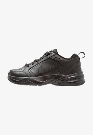 Zapatilla deportiva negra con parte superior de cuero y malla. Presenta puntera redonda, cierre de cordones en la parte delantera, cuello acolchado y suela texturizada para tracción.