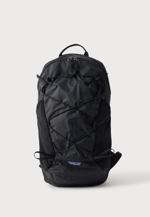 Sac à dos Patagonia noir avec cordon élastique à l'avant, poignée supérieure et bretelles rembourrées sur un fond clair uni.
