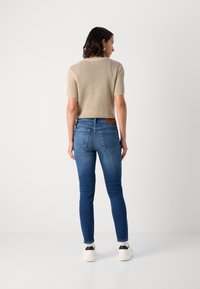 Béžový pletený krátky sveter s krátkymi rukávmi; modré denimové skinny džínsy; biele tenisky s čiernymi detailami na päte.