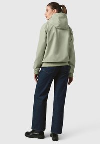 Jasnozielona bluza z kapturem i sznurkiem, zakończona ściągaczem, zestawiona z ciemnoniebieskimi dżinsami i czarnymi butami na sznurówki, widok z tyłu.