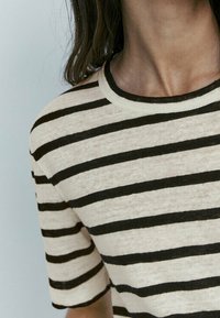 Randig t-shirt med horisontella svarta och krämfärgade ränder, rund halsringning, korta ärmar, tillverkad av lätt tyg med en mjuk textur.