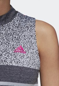 Débardeur de sport sans manches avec un motif tacheté noir et blanc, col montant et un logo Adidas rose sur le devant.