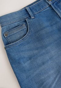 Jean en denim bleu présentant un design classique, cinq poches et des coutures contrastées. Le tissu a une texture lisse et un léger effet délavé.