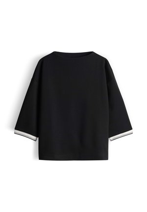 Top nero in misto cotone dalla vestibilità ampia, con maniche larghe e strisce bianche ai bordi dei polsini. Design semplice e pulito senza decorazioni.