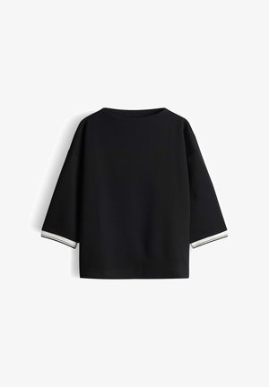 Haut noir en mélange de coton avec une coupe ample, manches larges et rayures blanches sur les bords des poignets. Design simple et épuré sans ornements.