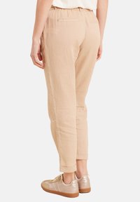 Beige Leinenmix-Hosen mit Kordelzugbund, schmal zulaufenden Beinen und umgeschlagenen Säumen. Kombiniert mit hellbeigen Sneakers.