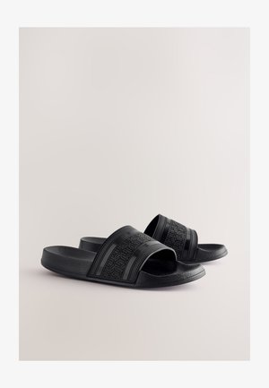 Mustat liukusandaalit, jotka on valmistettu kuvioidusta kumista. Niissä on kaksi leveää hihnaa geometrisin kuvioin ja muotoiltu pohja mukavuutta varten.