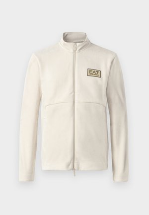 Veste en polaire zippée beige clair avec un col haut, présentant un petit logo EA7 noir et doré sur la poitrine et deux poches avant.