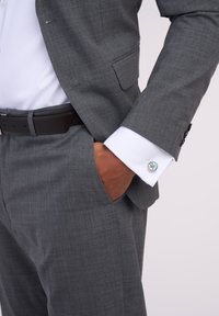 Gray suit with a textured fabric, white dress shirt, and a cufflink featuring a round, colorful design. Black belt completes the look.