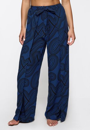 Weite blaue Hosen mit abstrakten schwarzen Wirbelmustern und einem gebundenen Bund, barfuß getragen.