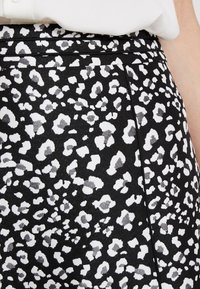 Jupe imprimé léopard en noir et blanc, avec une texture lisse, une coupe droite et un léger éclat ; comprend un détail à la taille.