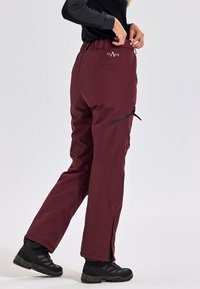 Pantaloni da neve bordeaux con vita elastica, due tasche laterali con zip e pantaloni con cerniere alle caviglie. Realizzati in materiale impermeabile, progettati per l'attività all'aperto.