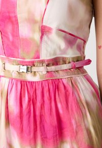 Robe à motifs rose et crème avec une jupe évasée, dotée d'une ceinture avec une boucle en argent, d'une texture froncée et d'un subtil dégradé de couleurs.