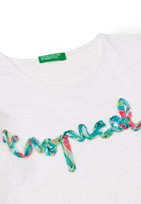 Camiseta blanca de algodón con una cinta colorida y texturizada en turquesa, rosa y verde formando la palabra "tropical" en el pecho.