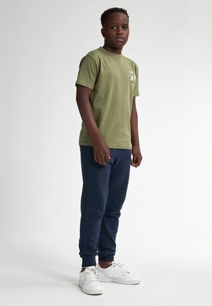 Olivgrön bomull t-shirt med en logotyp, kombinerad med marinblå sweatpants. Vita sportskor med texturerade sulor. Enkelt, avslappnat design.