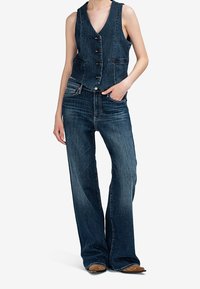 Denimová vesta s přiléhavým střihem, tmavá barva, pět knoflíků a boční kapsy, v kombinaci s širokými denimovými kalhotami tmavé barvy a hladkou texturou.