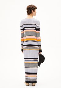 Lång, figurnära klänning med vertikala ribbor, prydd med flerfärgade ränder i grått, orange, rosa och marinblått. Långa ärmar, hållna med en svart mössa.