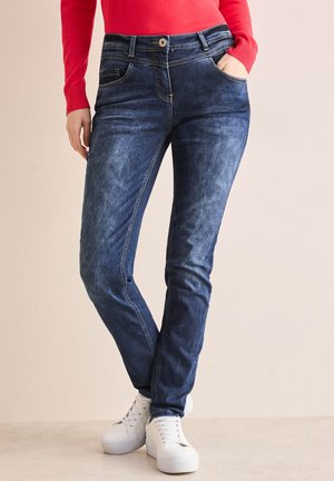 Donkerblauwe denim jeans met een vervaagde wassing, voorzien van vijf zakken, riemlussen en een knoopsluiting, gecombineerd met witte sneakers.