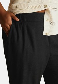 Svarta linnbyxor med elastisk midja, sidofickor och en slät yta. Matchas med en krämfärgad stickad topp med dekorativa knappar.