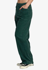 Gröna kordflosspants med rak bendesign, med framfickor och knappstängning. Matchas med svarta sneakers.