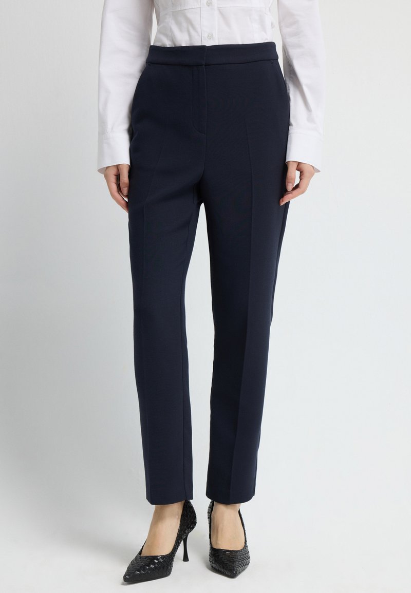 Námořnické kalhoty na míru s hladkým povrchem, obsahující vysoký pas a rovné nohavice, doplněné černými podpatky.