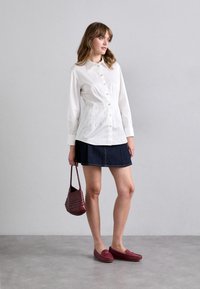 White button-up shirt with long sleeves, paired with a denim skirt. Accessories include a burgundy woven bag and matching slip-on shoes.