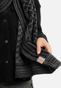 Zwarte en grijs gemusterde sjaal van zacht breiwerk, met geometrische ontwerpen en een label met het logo "Knit Factory."