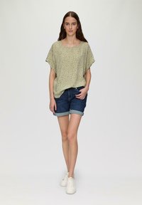 Haut à manches courtes, vert pâle avec un motif blanc, associé à un short en denim foncé. Le mannequin porte des baskets blanches. Design simple et coupe décontractée.
