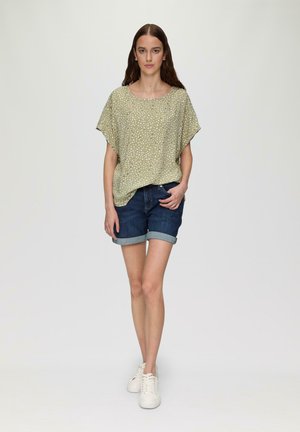 Haut à manches courtes, vert pâle avec un motif blanc, associé à un short en denim foncé. Le mannequin porte des baskets blanches. Design simple et coupe décontractée.