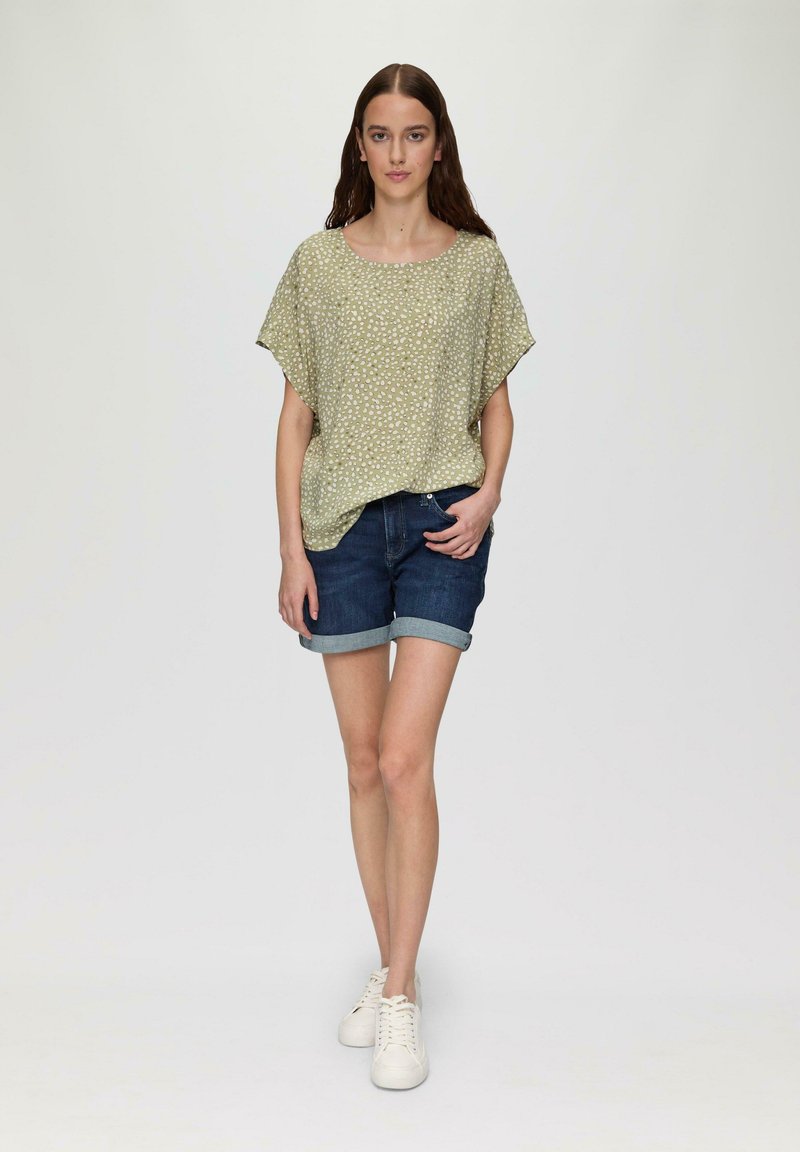 Haut à manches courtes, vert pâle avec un motif blanc, associé à un short en denim foncé. Le mannequin porte des baskets blanches. Design simple et coupe décontractée.