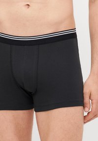 Black boxer shorts with a fitted design, made of soft fabric, featuring a black and white striped elastic waistband.
