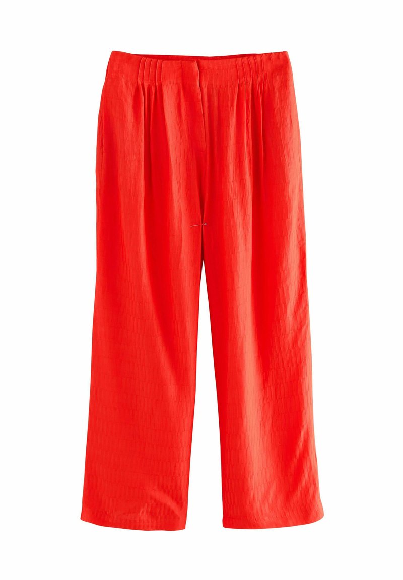 Pantalons larges rouges avec une surface texturée, dotés d'une taille élastique et d'une coupe décontractée. Pas de matériel ou d'accents visibles.