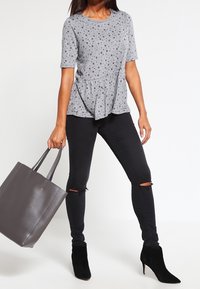 Top peplum gris con puntos blancos y mangas cortas, combinado con jeans negros ajustados con rodilleras rasgadas y botas negras hasta el tobillo. Bolsa de mano gris.
