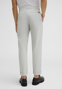 Pantaloni grigi chiari con una finitura texturizzata, caratterizzati da un design a gamba dritta, orli arrotolati e un'etichetta nera in vita. Scarpe nere visibili.