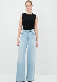 Top negro sin mangas; jeans de pierna ancha de tono azul claro con cintura alta; denim de lavado claro; costuras visibles y bolsillos frontales; diseño minimalista.