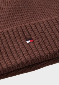 Bonnet en tricot ribbé marron avec une petite étiquette de logo tricolore en bleu, blanc et rouge. Texture douce et coupe ajustée pour la chaleur.