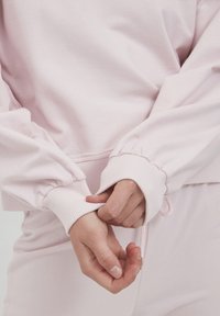 Sudadera rosa chiaro con maniche a palloncino elasticizzate, polsini a coste e una vestibilità rilassata. Tessuto morbido e testurizzato con un design informale.