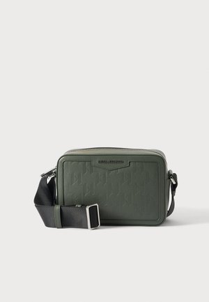 Kleine rechthoekige groene crossbodytas met reliëfpatroon, zwarte verstelbare riem en zilveren ritssluiting op effen achtergrond.