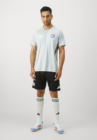 Lys grå idrettsdrakt med svarte shorts, med logo og striper, kombinert med hvite knelengde sokker og blå fotballsko.