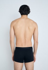 Schwarze Boxerbriefs aus glattem Stoff, mit einem schmalen Bund. Das Modell wird von hinten betrachtet und zeigt ein schlichtes Design.