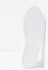 Vit gummisula med vågig textur, med präglat märke "Polo Ralph Lauren" i mitten och minimalistisk design.