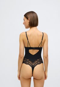 Μαύρο κορμάκι με συνδυασμό λείου υφάσματος και φλοράλ δαντέλας, με χαμηλή πλάτη και ρυθμιζόμενους ιμάντες. Στυλ κορδονιού με λεπτομέρειες κοψίματος.