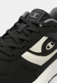 Black sneaker with mesh and synthetic upper, featuring grey accents, round toe, and prominent logo detail on the side and tongue.