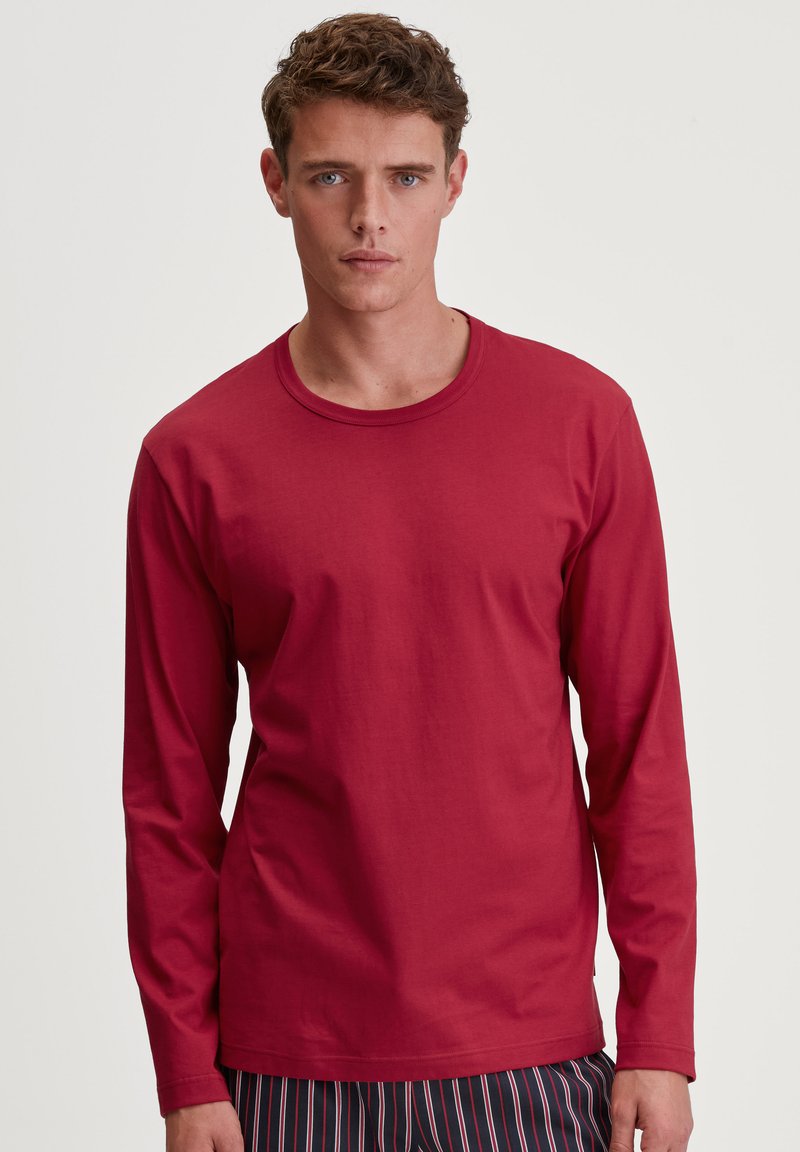 Langarm, ronde hals t-shirt van dieprode katoen. Heeft een ontspannen pasvorm en een gladde textuur, gecombineerd met gestreepte pyjamabroeken.