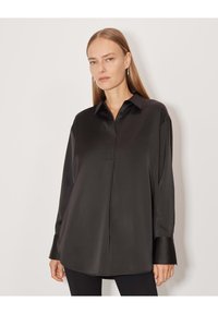 Blusa nera in satin con colletto a punta e maniche lunghe, caratterizzata da un taglio dritto e un leggero lucido. Design elegante con una texture morbida.