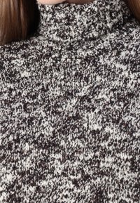 Rollkragenpullover aus strukturiertem Strick mit einem melierten Muster in Schwarz, Braun und Creme. Hoher Kragen und mittleres Stoffgewicht.