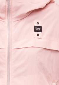 Ροζ ανοιχτόχρωμο μπουφάν με φερμουάρ μπροστά και μαύρη ορθογώνια ετικέτα επωνυμίας με την επιγραφή "Blauer U.S.A.", στερεωμένη με δύο μεταλλικά καρφιά πάνω και κάτω.